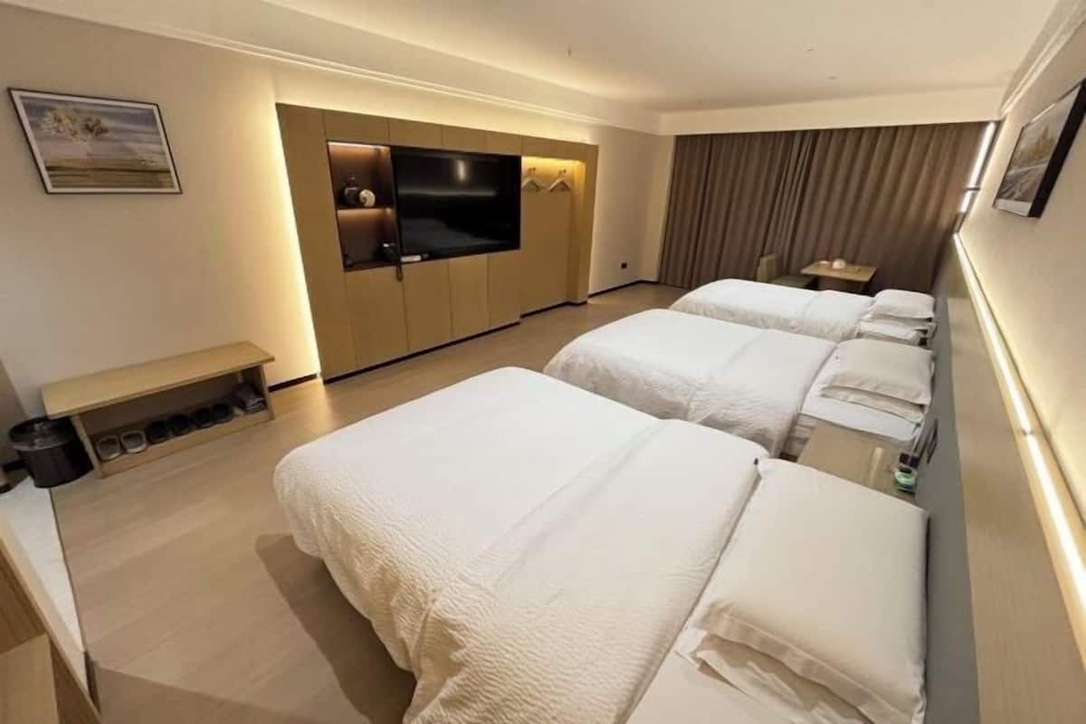A hotel room with two beds, a TV, a bench, and a small table.