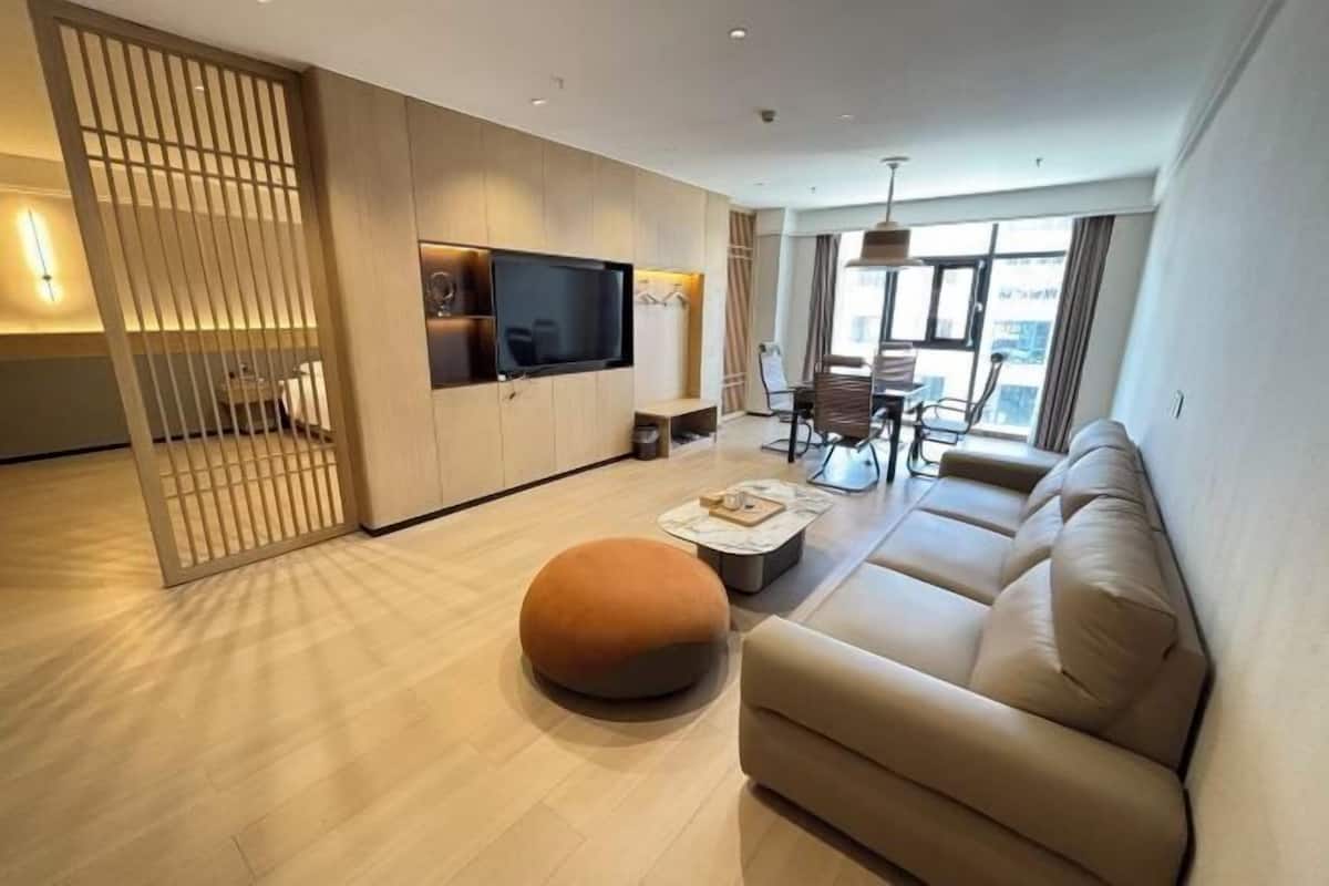 A modern living room with a sofa, ottoman, TV, and a dining area with chairs and a table.