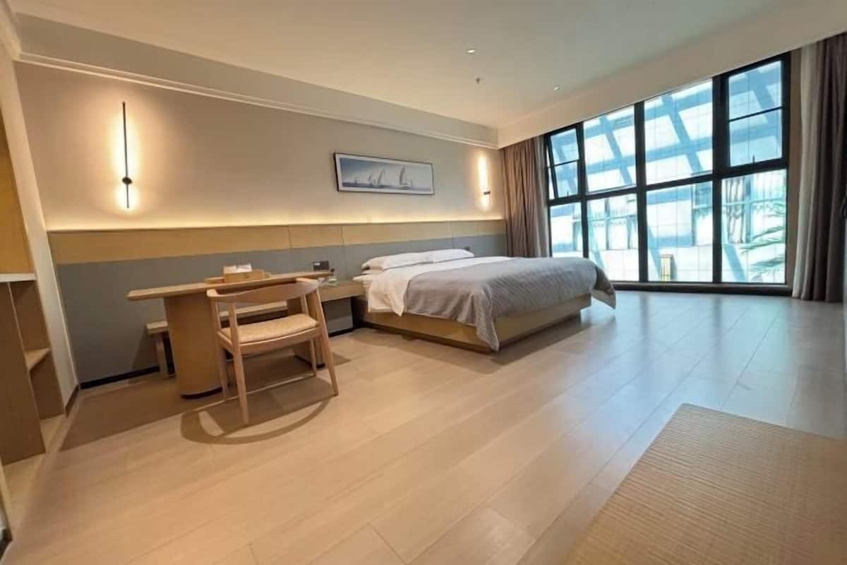 A hotel room with a bed, desk, chair, and large windows.