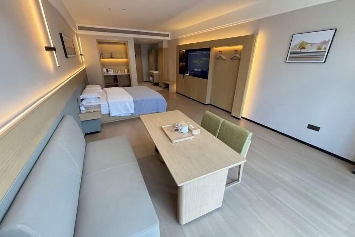 A modern hotel room with a sofa, a small table, a bed, a TV, and a bathroom.