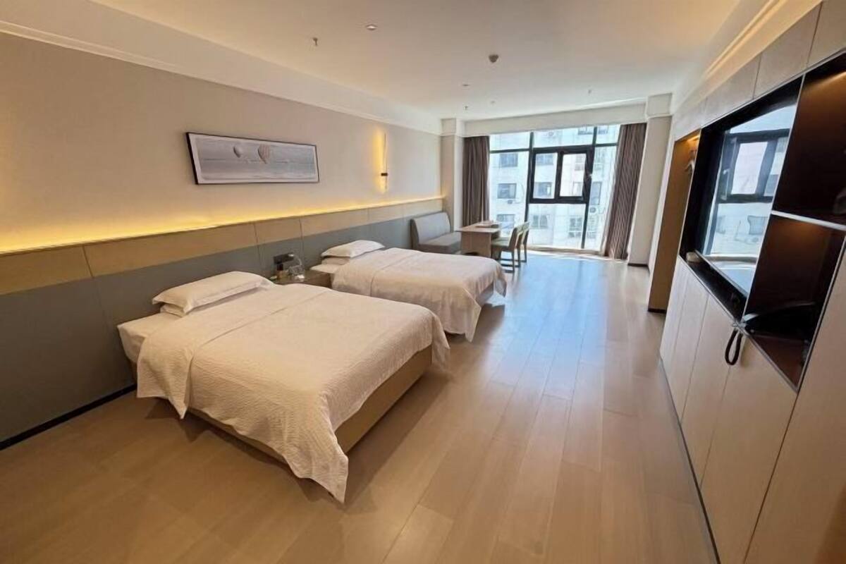A hotel room with two beds, a desk, and a large window.