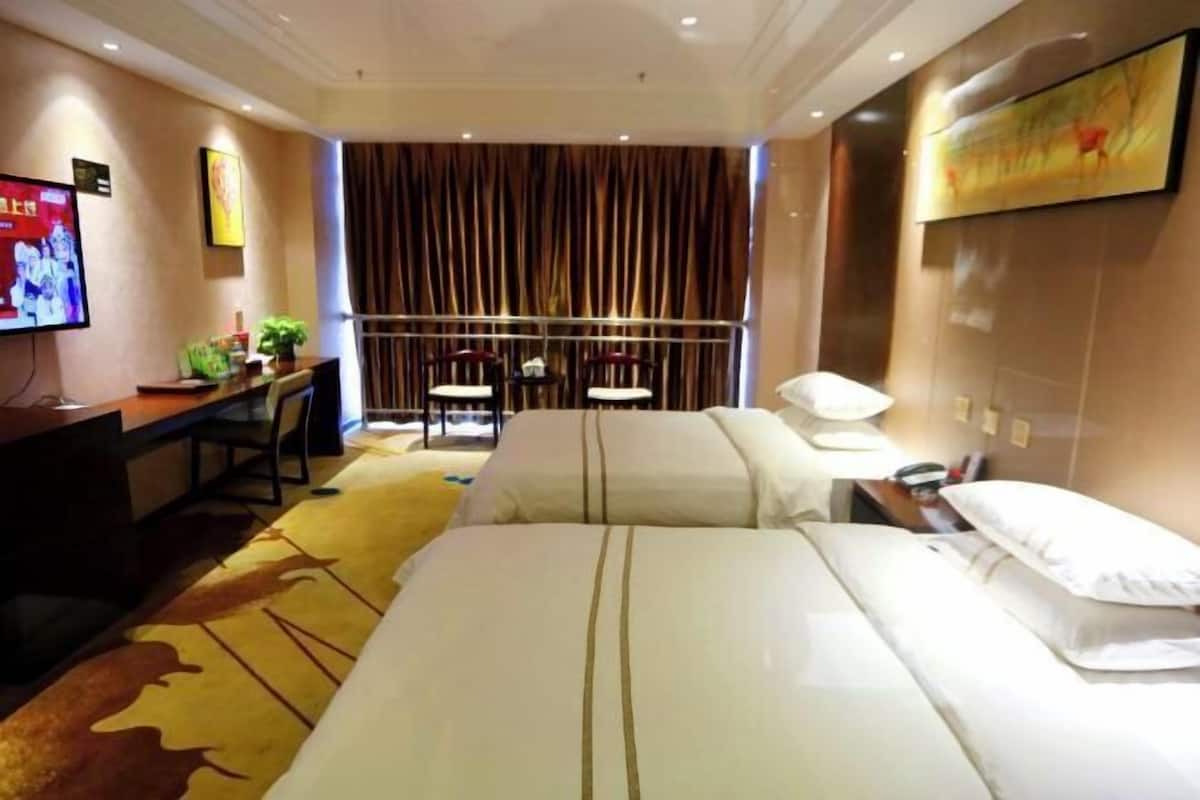 A hotel room with two beds, a desk with a chair, a TV, and a curtain backdrop.