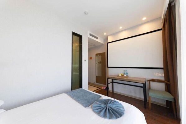 A hotel room with a bed, a desk, a chair, and a large window.