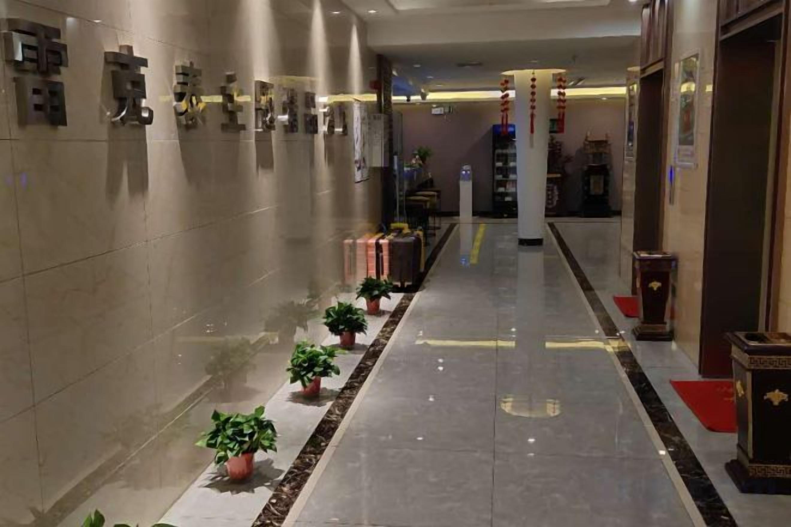 A hotel lobby with a long corridor, potted plants, and a reception desk.