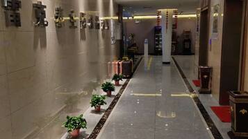 A hotel lobby with a long corridor, potted plants, and a reception desk.