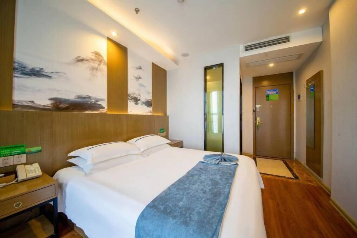 A hotel room with a bed, bedside table, and a wall-mounted artwork.