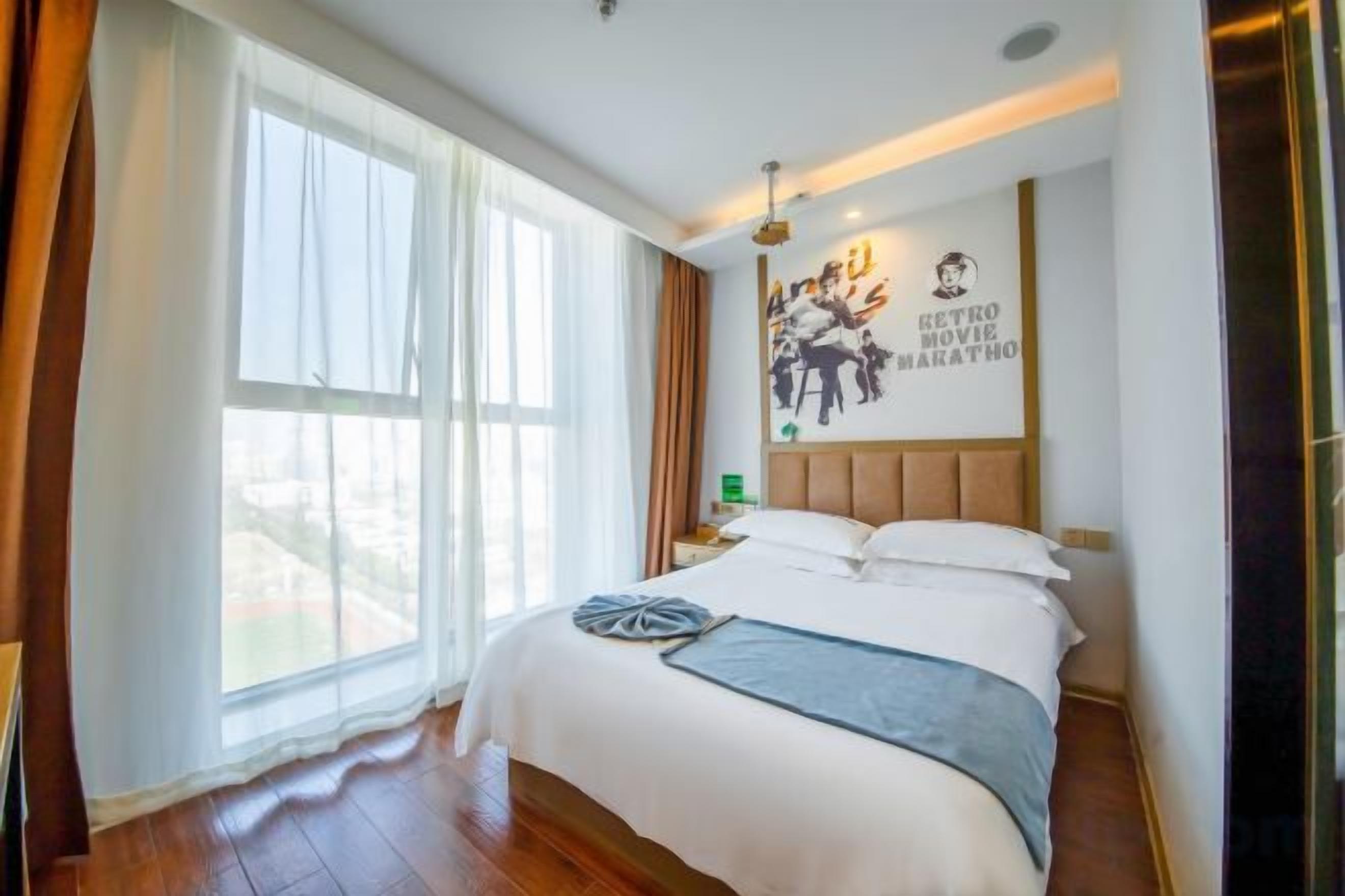 A hotel room with a large bed, a nightstand, a wall clock, and a window with curtains.