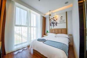 A hotel room with a large bed, a nightstand, a wall clock, and a window with curtains.