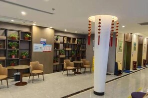 Um saguão de hotel com áreas de estar, balcão de recepção e um pilar com decorações penduradas.