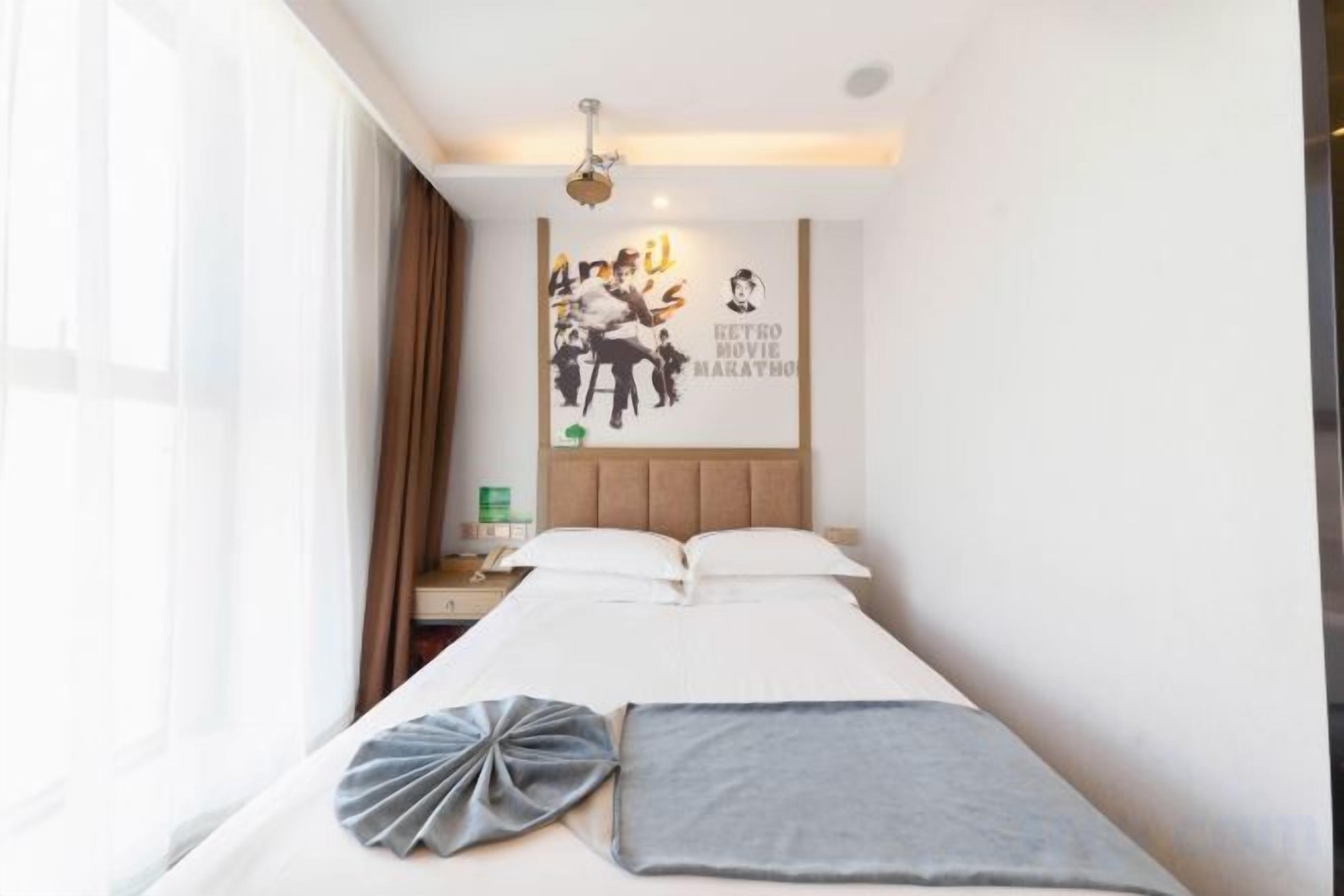 Une chambre d’hôtel avec un lit, une table de chevet, une horloge murale et une affiche.