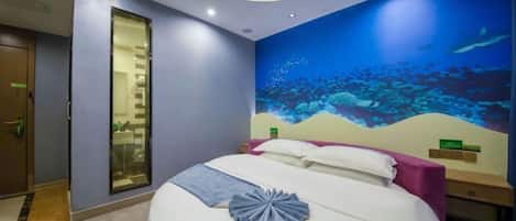 A hotel room with a bed, a circular ceiling light, a wall mural of an underwater scene, and a door with a glass panel.