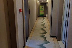 Een hotelgangen met een patroon vloerkleed, deuren aan beide zijden en een groen bord in de verte.