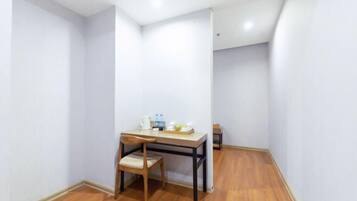A small room with a wooden floor, a table with a chair, and a bed in the corner.