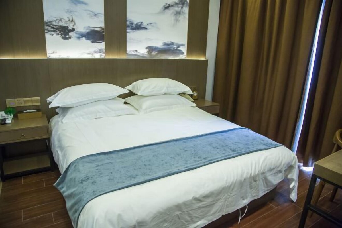 Ein Hotelzimmer mit einem großen Bett, einem Nachttisch mit Lampe und einem Fenster mit Vorhängen.