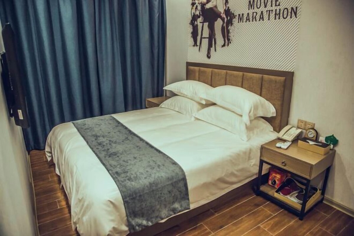 Ein ordentlich bezogenes Bett mit grauer Decke, einem hölzernen Kopfteil und einem Nachttisch mit Telefon und Uhr.