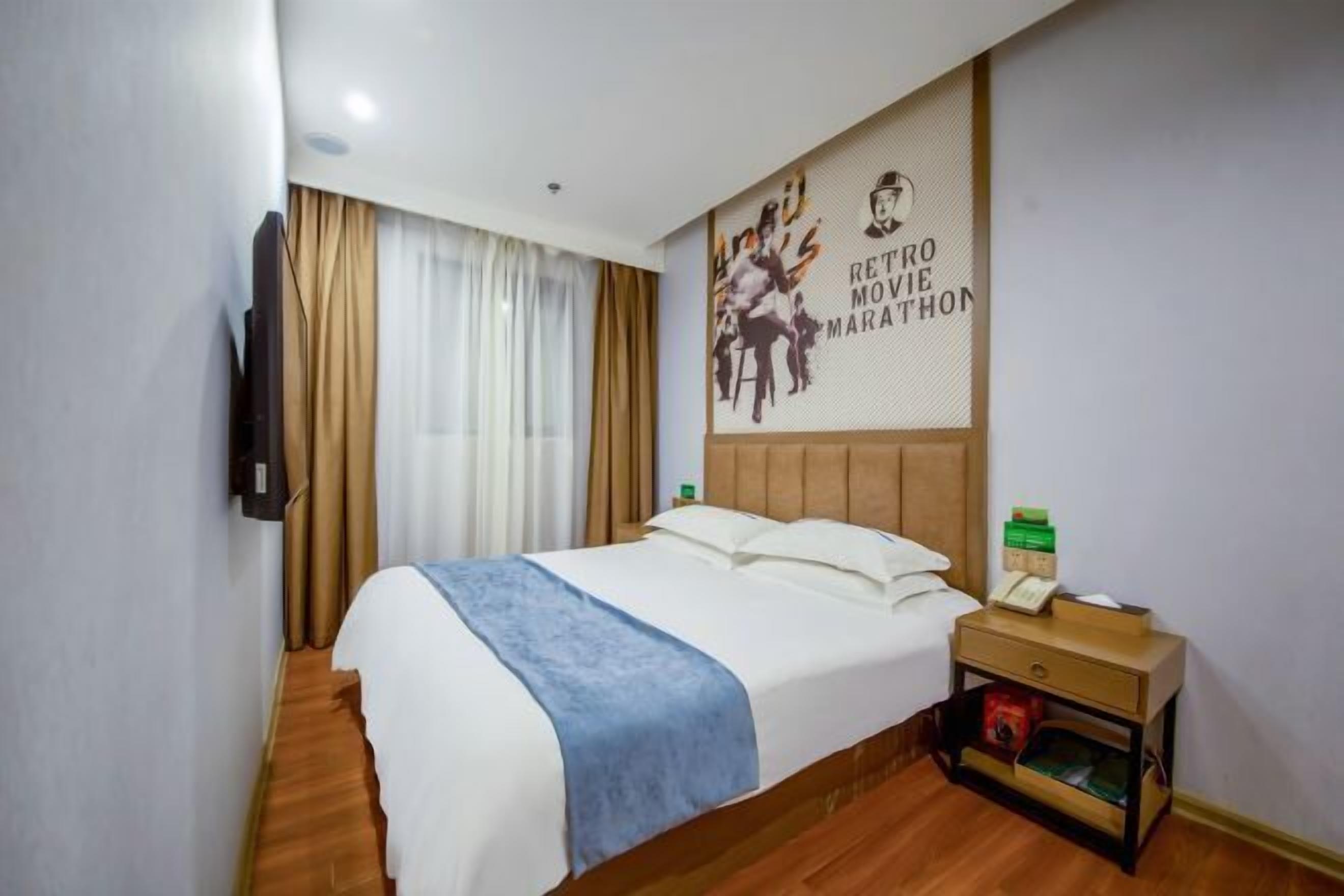 Una habitación de hotel con cama, mesita de noche, televisión montada en la pared y un cartel.