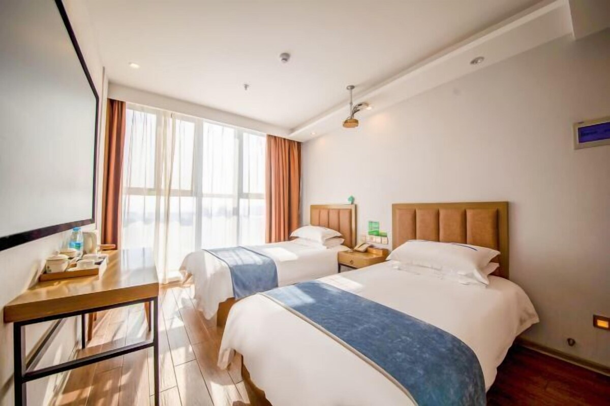 Ein Hotelzimmer mit zwei Betten, einem Schreibtisch und einem großen Fenster mit Vorhängen.