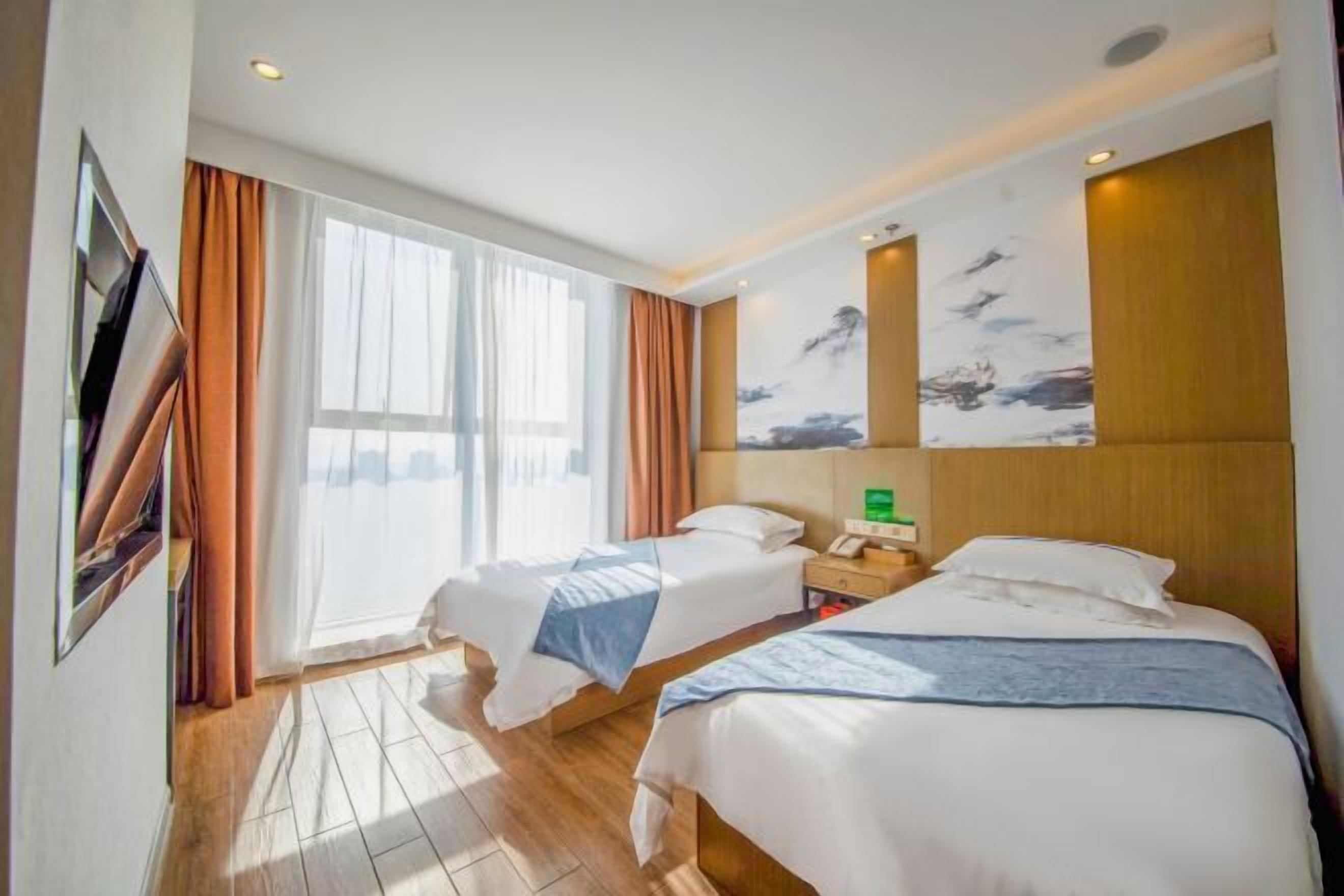 Habitación de hotel con dos camas, un ventanal con cortinas, un cuadro en la pared y suelo de madera.