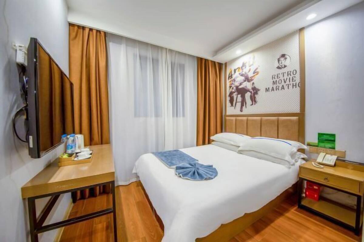 A hotel room with a bed, a bedside table, a TV, and a wall with a poster.