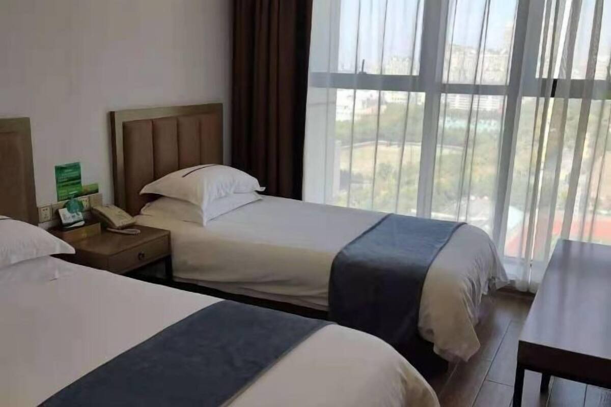 A hotel room with two beds, a nightstand with a phone, a window with curtains, and a view of the outside.