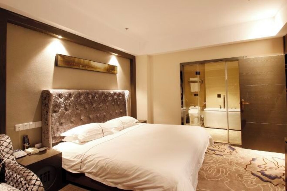Une chambre d’hôtel avec un grand lit, une table de chevet, un miroir et une salle de bain visible à travers une porte ouverte.