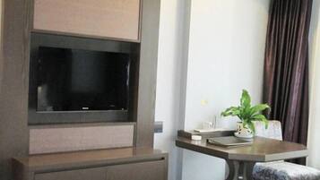 A modern room with a flat-screen TV mounted on a wooden cabinet, a small table with a plant, and a cushioned chair.