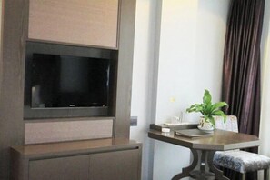 Una habitación moderna con un televisor de pantalla plana montado en un mueble de madera, una mesita con una planta y un sillón acolchado.