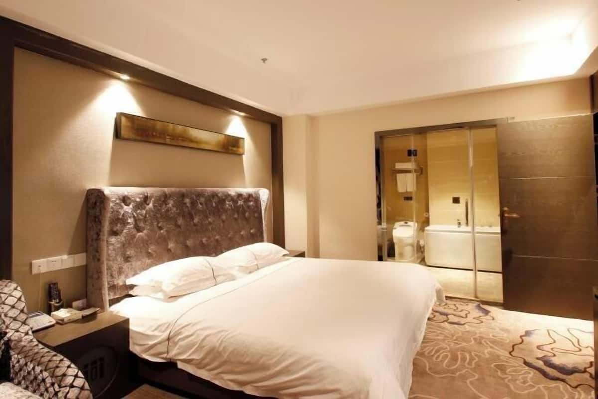 A hotel room with a large bed, a nightstand, a mirror, and a bathroom visible through an open door.