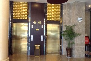 A hotel lobby with two elevators, a reception desk, and a potted plant. - Shuiyuan Shangmei Hotel (Bengbu)