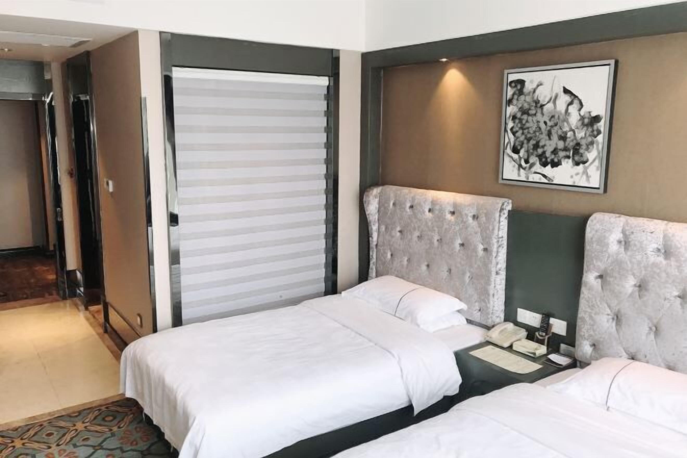 Habitación de hotel con dos camas, un ventanal grande, una puerta y una obra de arte colgada en la pared.