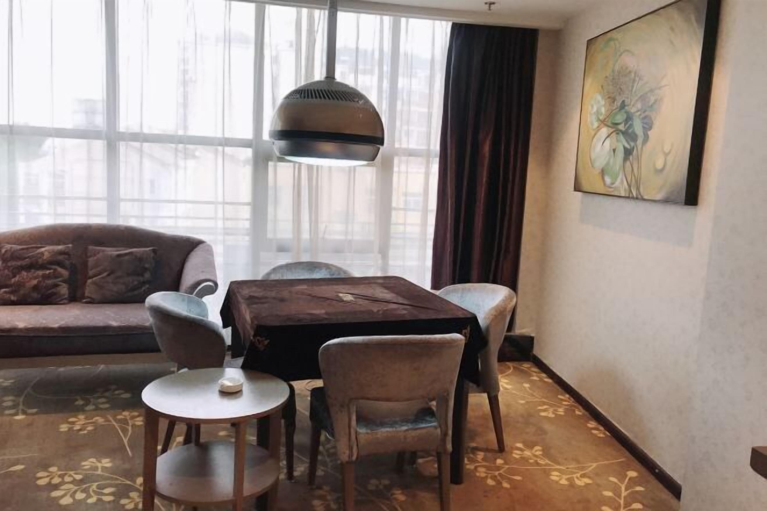 A room with a sofa, a table with chairs, a hanging light fixture, and a painting on the wall.