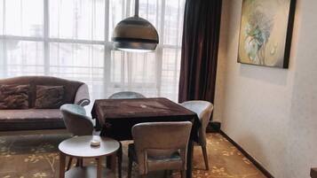A room with a sofa, a table with chairs, a hanging light fixture, and a painting on the wall.