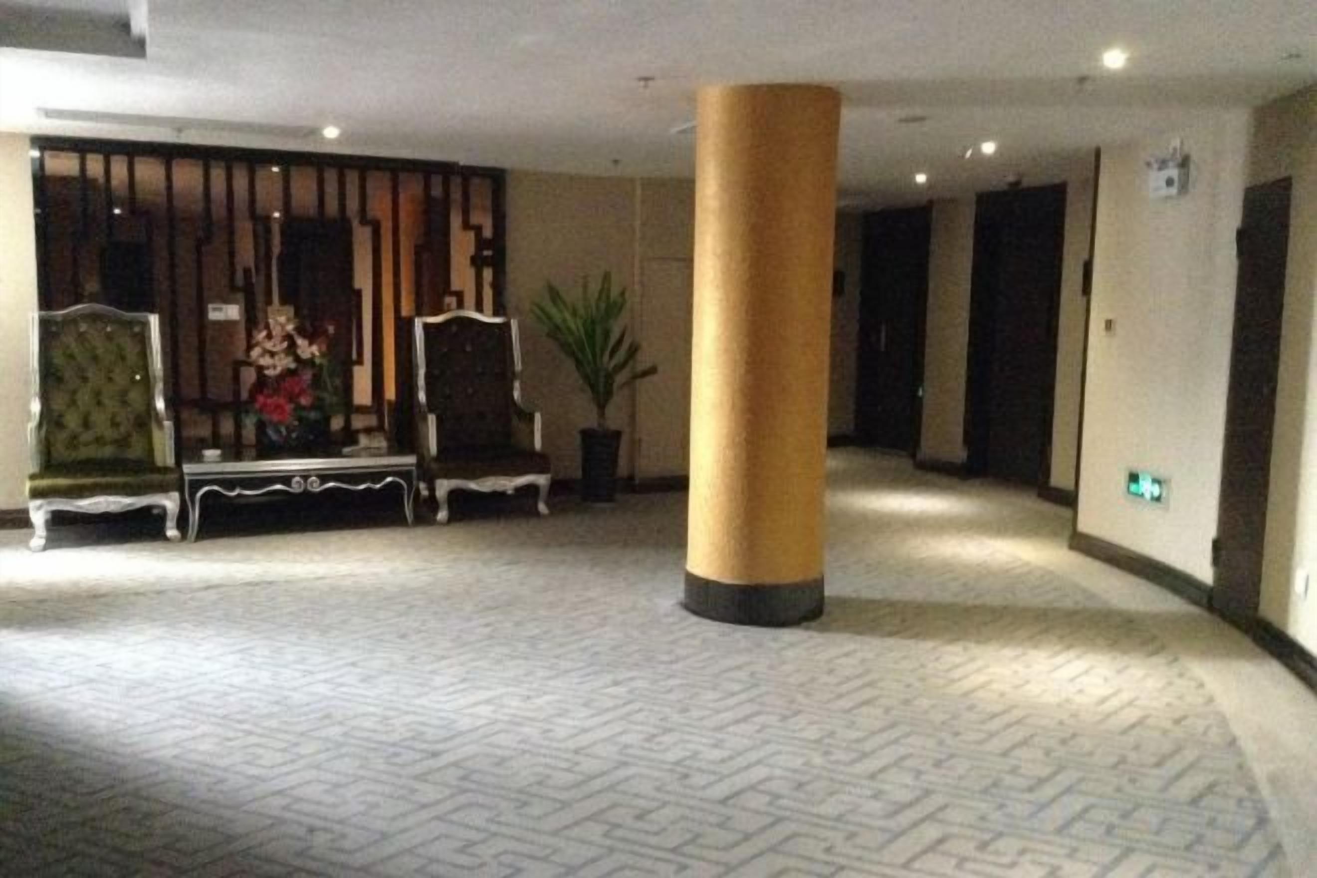 Een hotellobby met een kamerbreed tapijt, een grote zuil en twee gestoffeerde fauteuils.