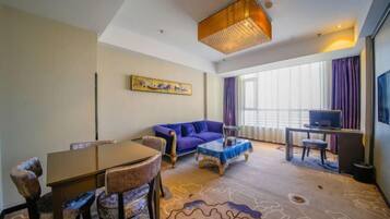 A hotel room with a dining table, chairs, a sofa, a TV, and a large window with curtains.