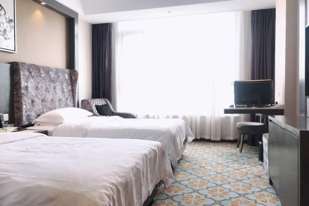 A hotel room with two beds, a desk with a television, a chair, and a patterned floor.