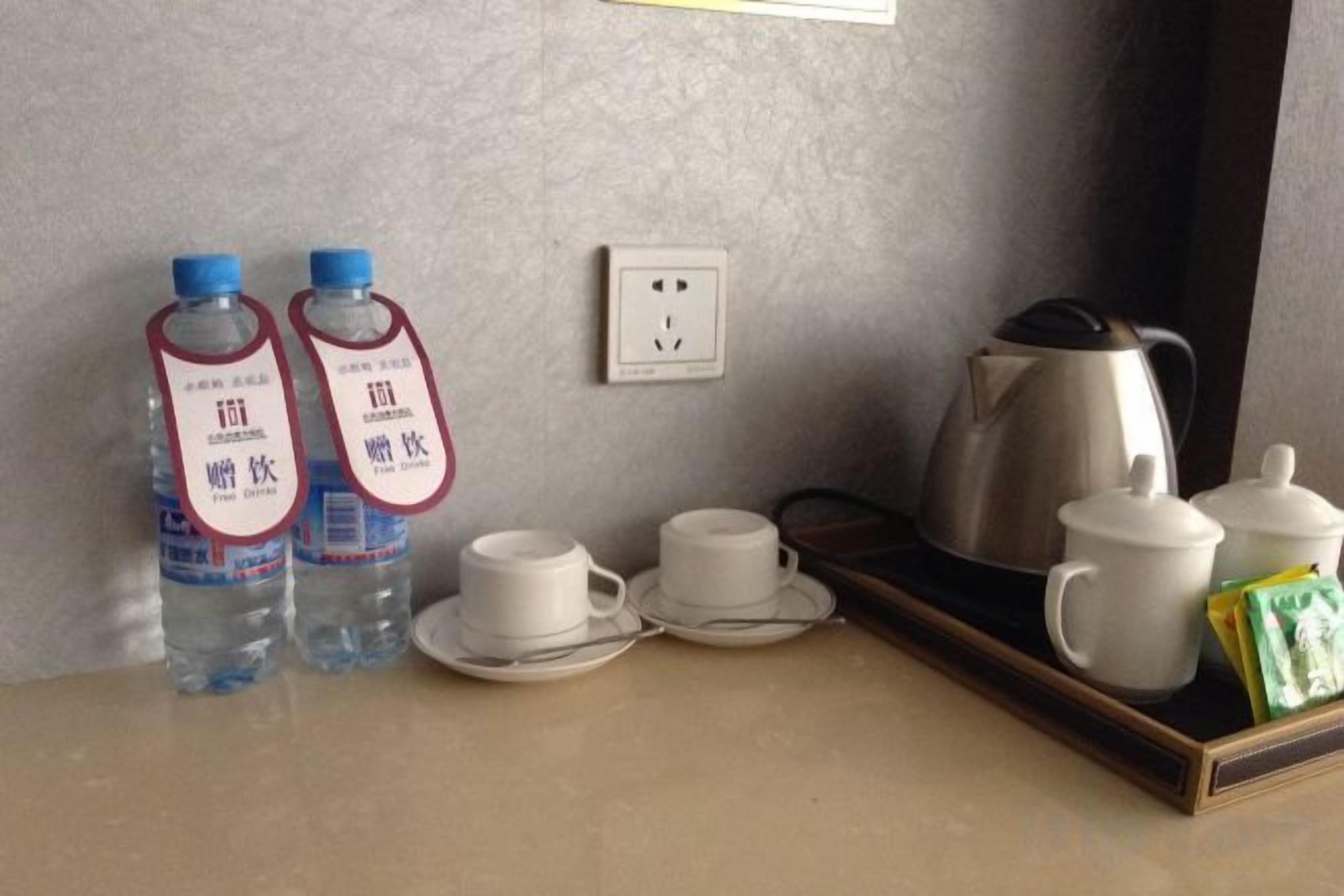 A hotel room with a coffee maker, two water bottles, two cups, and a tray with a teapot and cups.