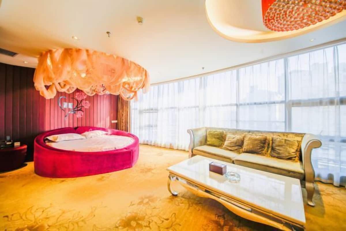 A modern living room with a red circular sofa, a glass coffee table, and a beige sofa with cushions.