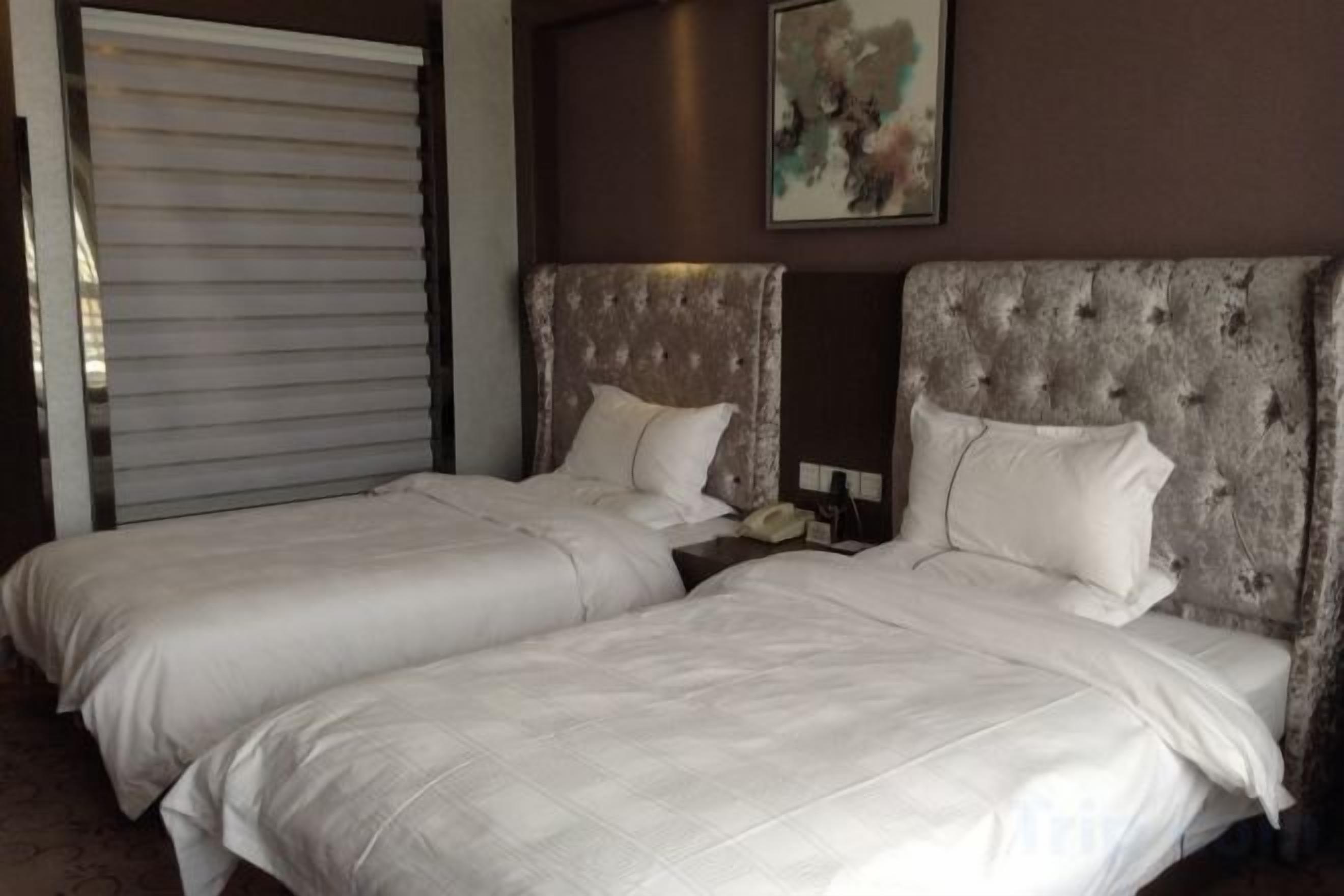 A hotel room with two beds, a large window with blinds, and a painting on the wall.
