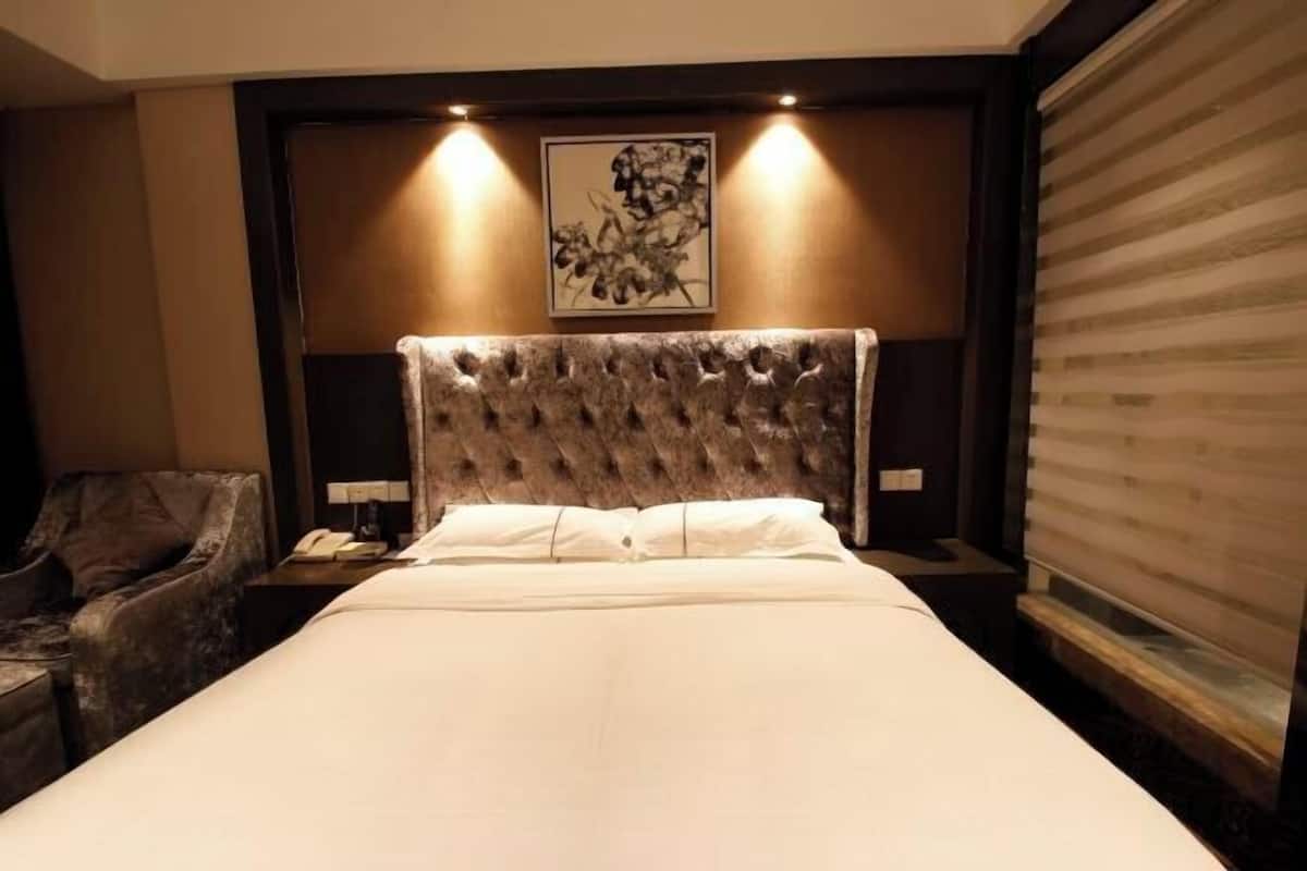 A hotel room with a large bed, a headboard, a chair, a bedside table with a lamp, and a painting on the wall.