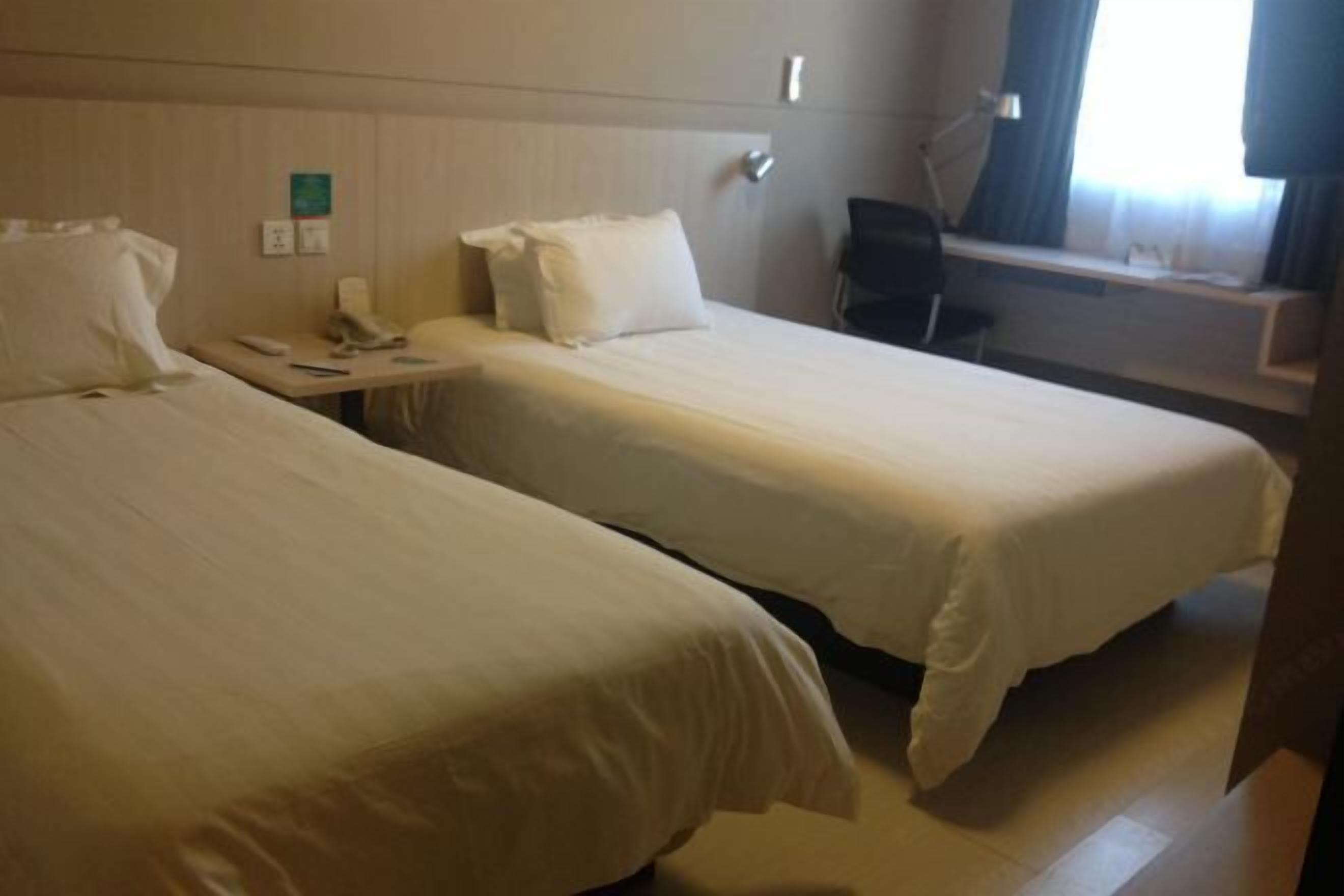 A hotel room with two single beds, a desk with a chair, a phone, and a window with curtains.