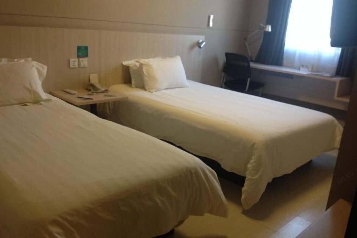 A hotel room with two single beds, a desk with a chair, a phone, and a window with curtains.