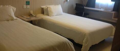 A hotel room with two single beds, a desk with a chair, a phone, and a window with curtains.