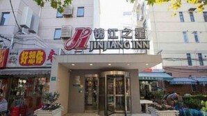 A hotel entrance with a revolving door, a sign with Chinese characters, and a storefront with a red awning in the background.
