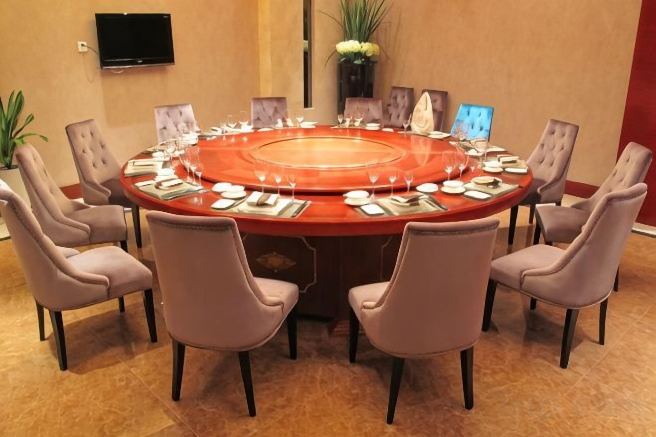 A round table with chairs, a flat-screen TV, and a vase with flowers.