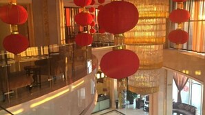Un hall d’entrée spacieux, doté d’un plafond haut, de grands lustres et de décorations rouges suspendues.
