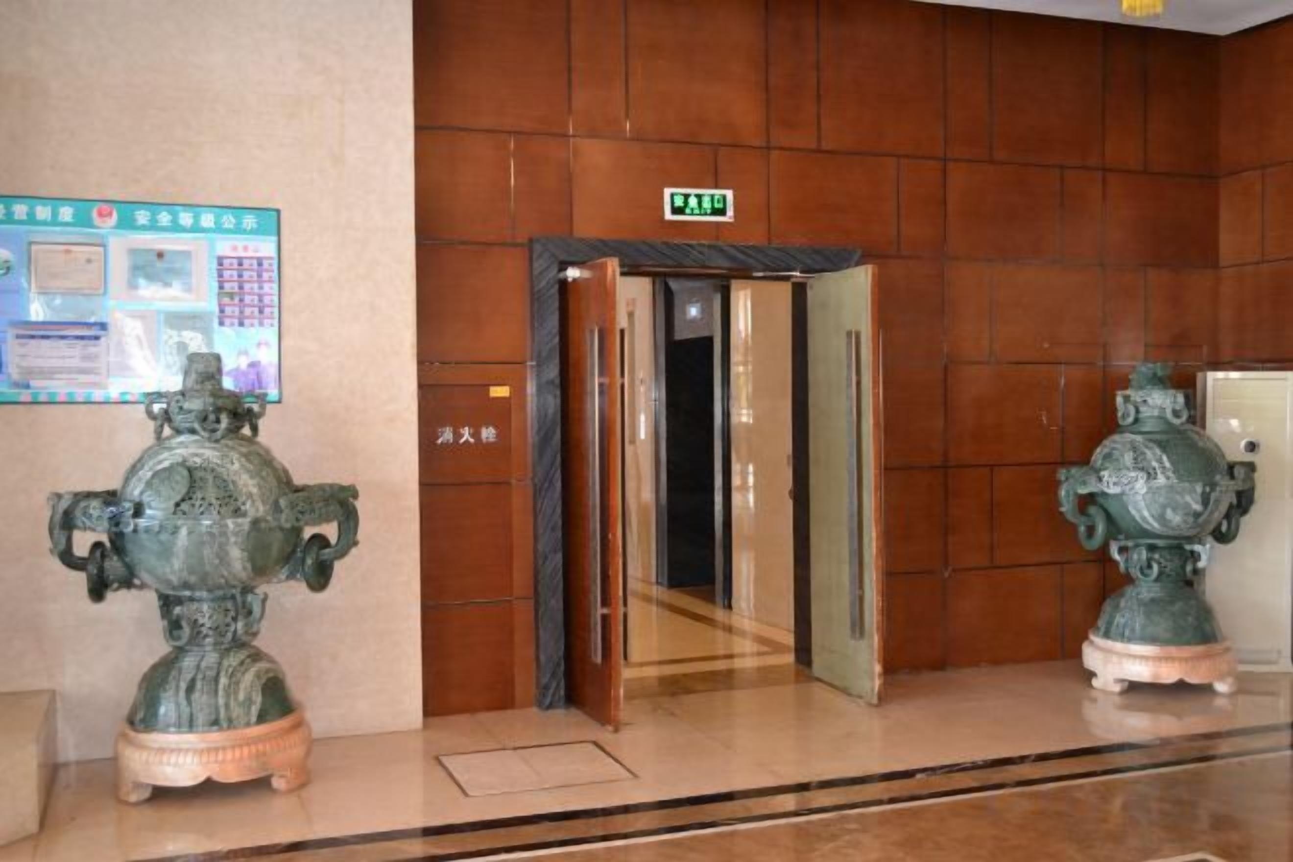 Un hall d’entrée avec un mur en bois, une enseigne de sortie verte et deux statues vertes.