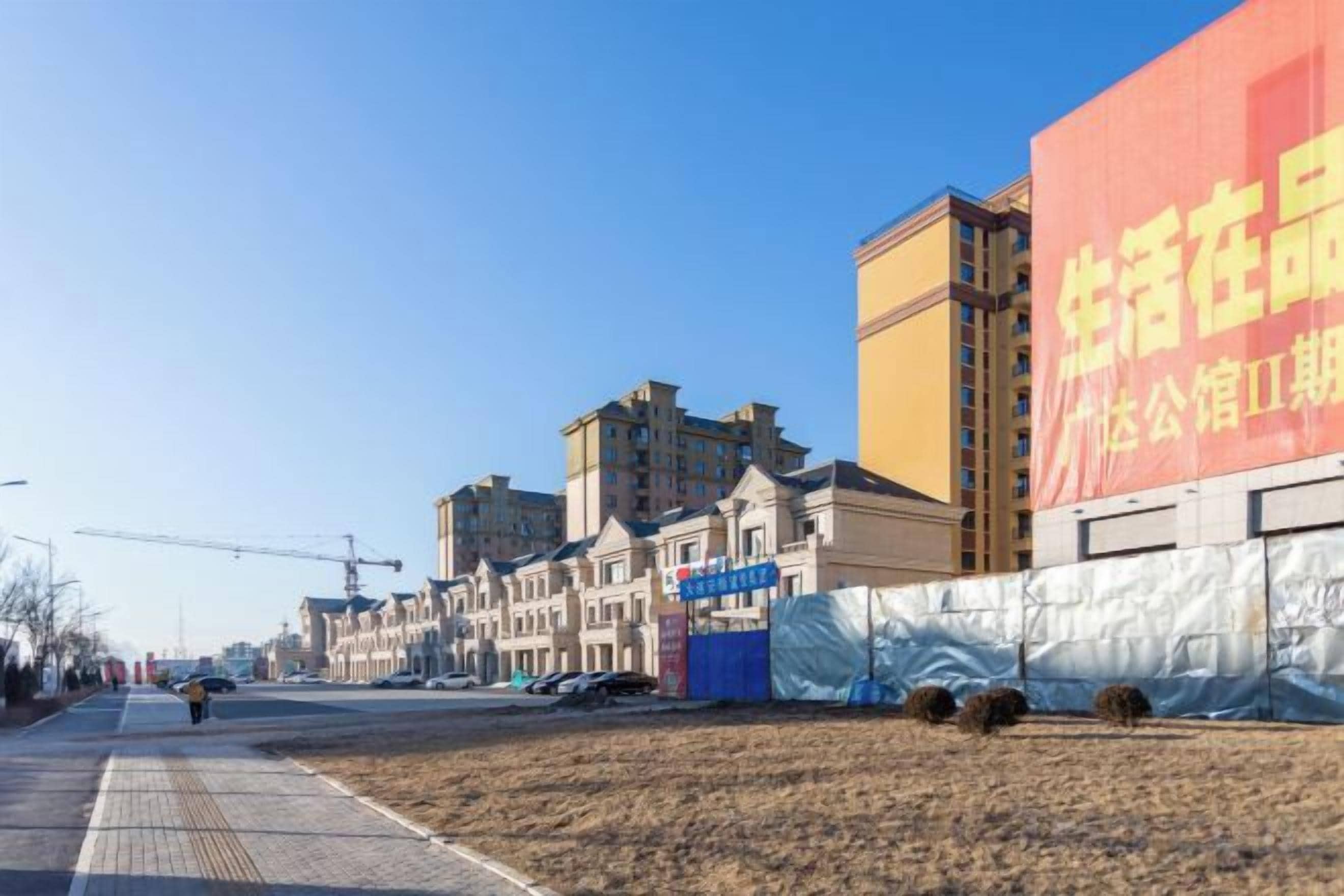 Una calle con edificios, una obra en construcción y un cartel rojo grande.