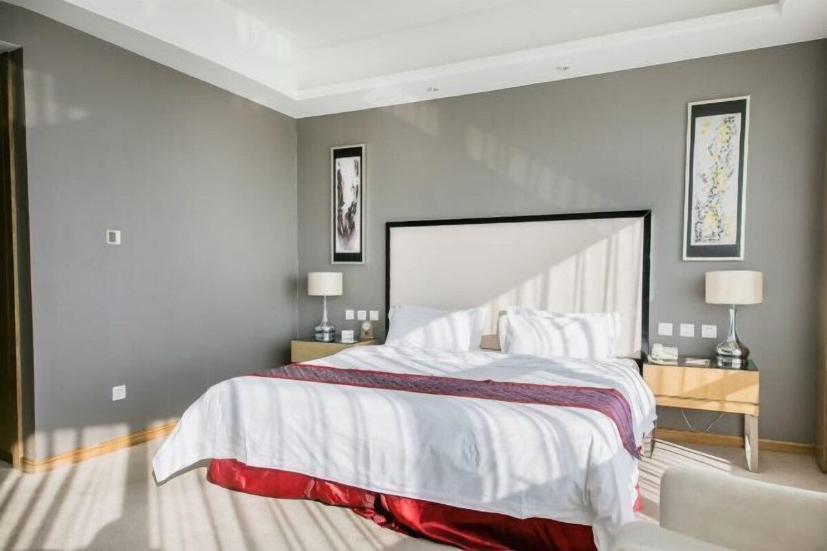 A modern hotel room with a large bed, bedside tables, and artwork on the walls.