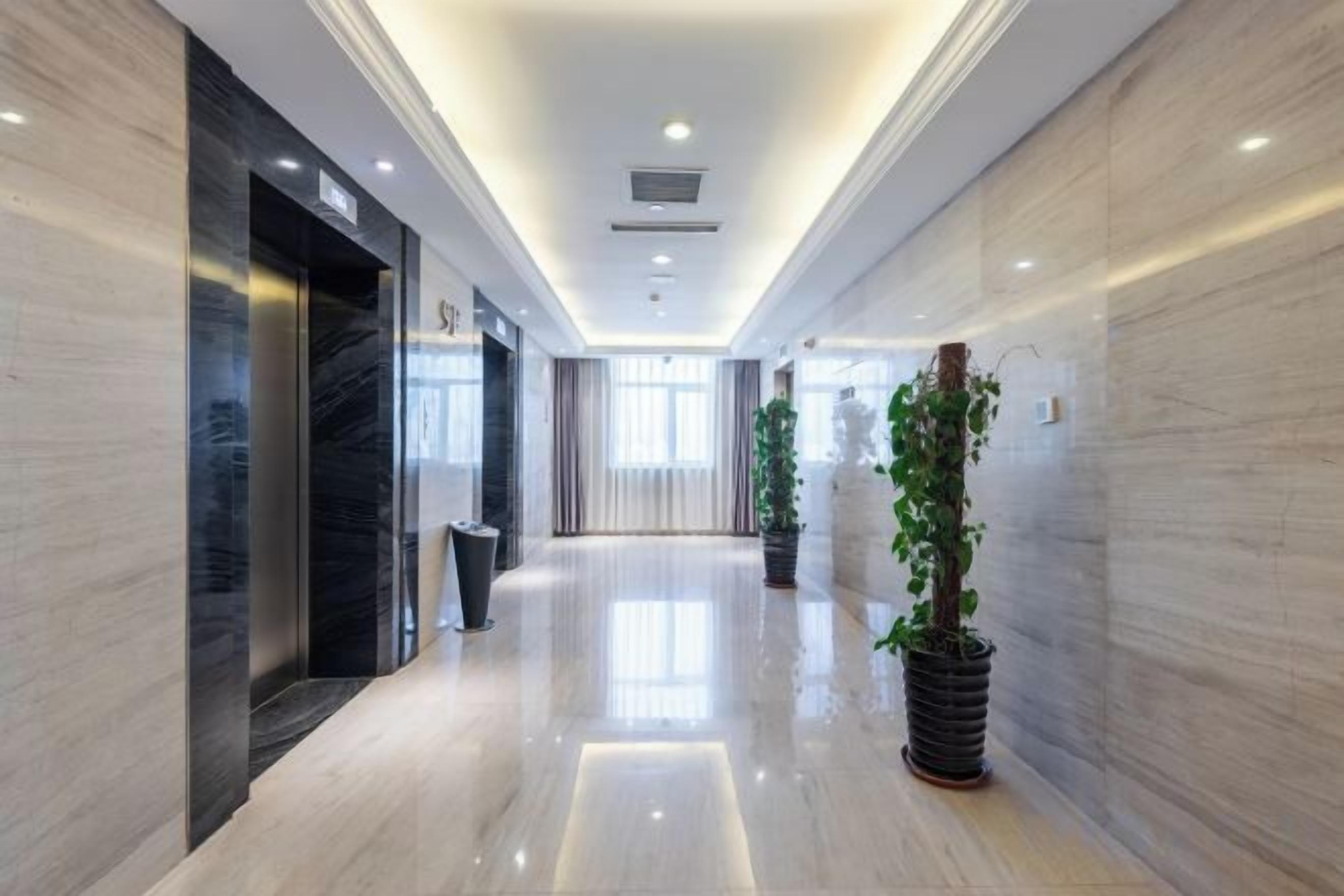 Un pasillo de hotel con piso de mármol, una planta en maceta y una zona de recepción con un cartel.