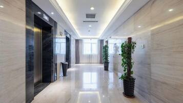 Un pasillo de hotel con piso de mármol, una planta en maceta y una zona de recepción con un cartel.